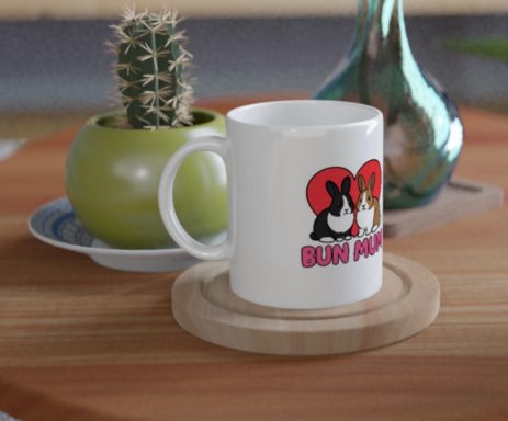 Bun Mug White mug with cartoon dogs, placed on a wooden coaster beside a green pot and cactus.